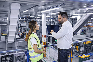 A female and a male Leadec employee with a laptop talking in a production facility.