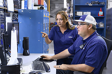 Two Leadec employees check inventory of spare parts at computer